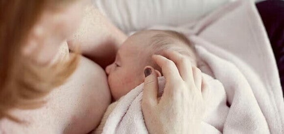 Ένα μωρό σκεπασμένο με κουβερτάκι ενώ θηλάζει στην αγκαλιά της μητέρας του. 